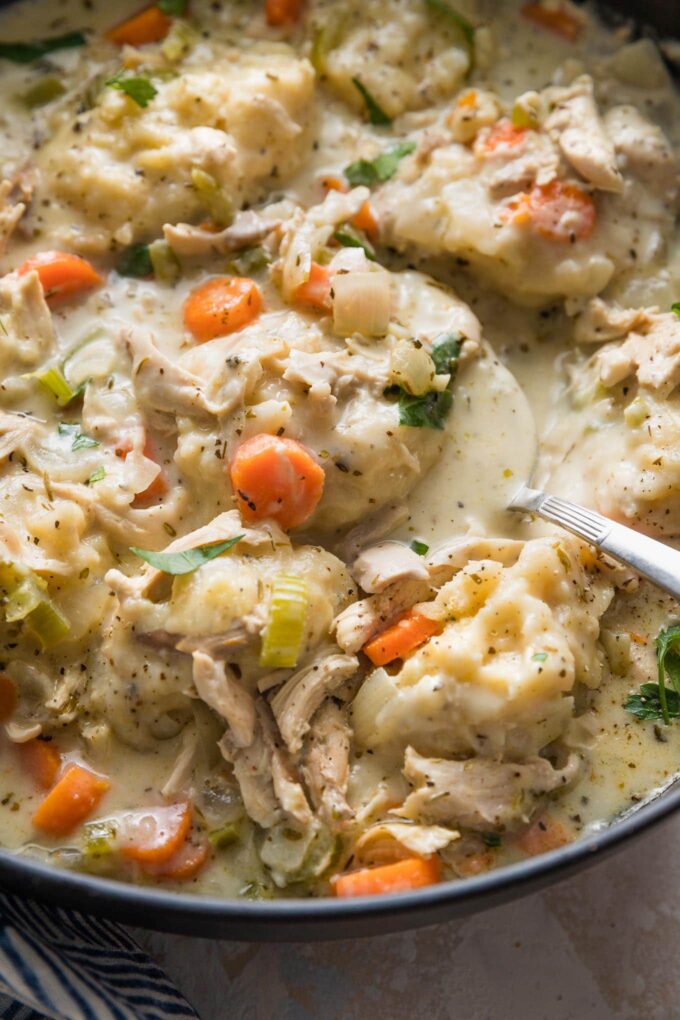 Angled view of a spoon holding broth and a dumpling in a deep sided pan.