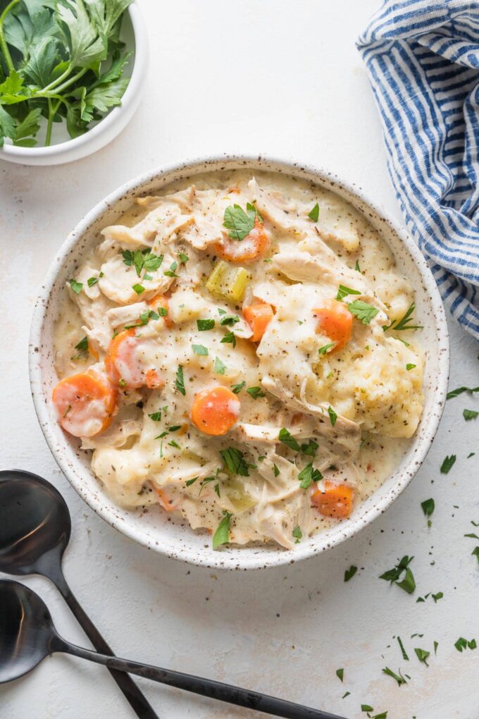 Overhead view of a shallow bowl filled with a serving of warm chicken and dumplings garnished with fresh Italian parsley.