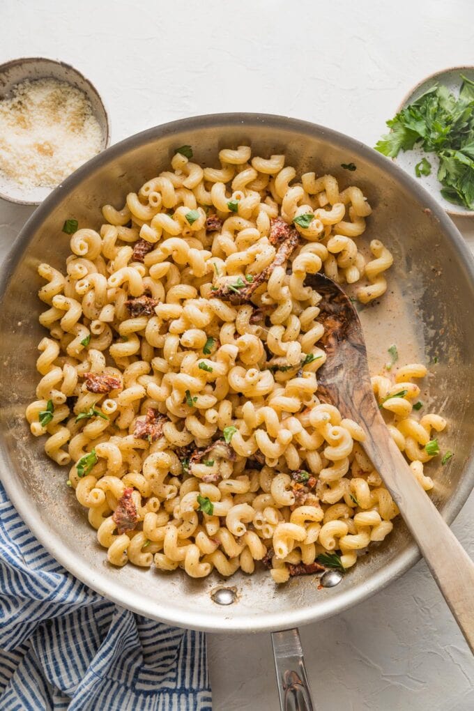A wooden spoon scraping out a serving of cavatappi pasta from a skillet.