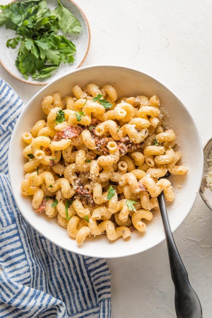 Small white bowl filled with a serving of cavatappi pasta in a light cream sauce with sun-dried tomatoes, Parmesan, and a garnish of fresh parsley.