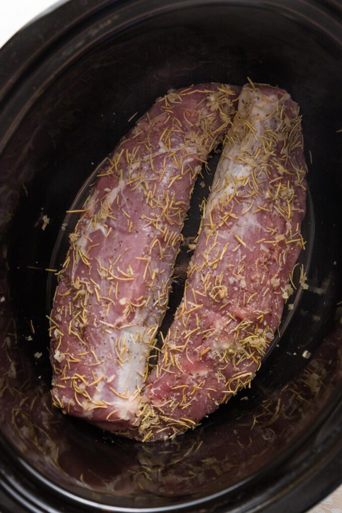Pork tenderloin with a spice rub resting in a slow cooker, ready to cook.