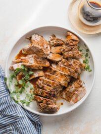 Pork tenderloin cooked with a balsamic glaze, sliced into medallions, and presented on a platter with a garnish of fresh oregano and extra glaze in the background.