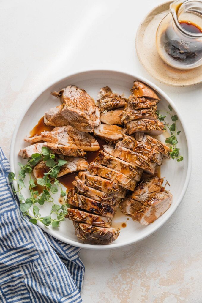 Pork tenderloin cooked with a balsamic glaze, sliced into medallions, and presented on a platter with a garnish of fresh oregano and extra glaze in the background.
