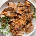 Pork tenderloin cooked with a balsamic glaze, sliced into medallions, and presented on a platter with a garnish of fresh oregano.