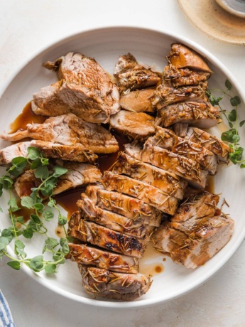 Pork tenderloin cooked with a balsamic glaze, sliced into medallions, and presented on a platter with a garnish of fresh oregano.