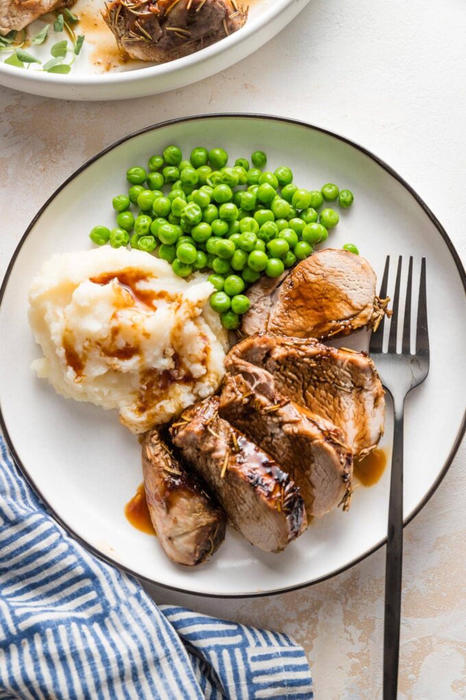 Small plate with a dinner sized-portion of balsamic pork tenderloin, mashed potatoes, and peas with balsamic glaze over everything.