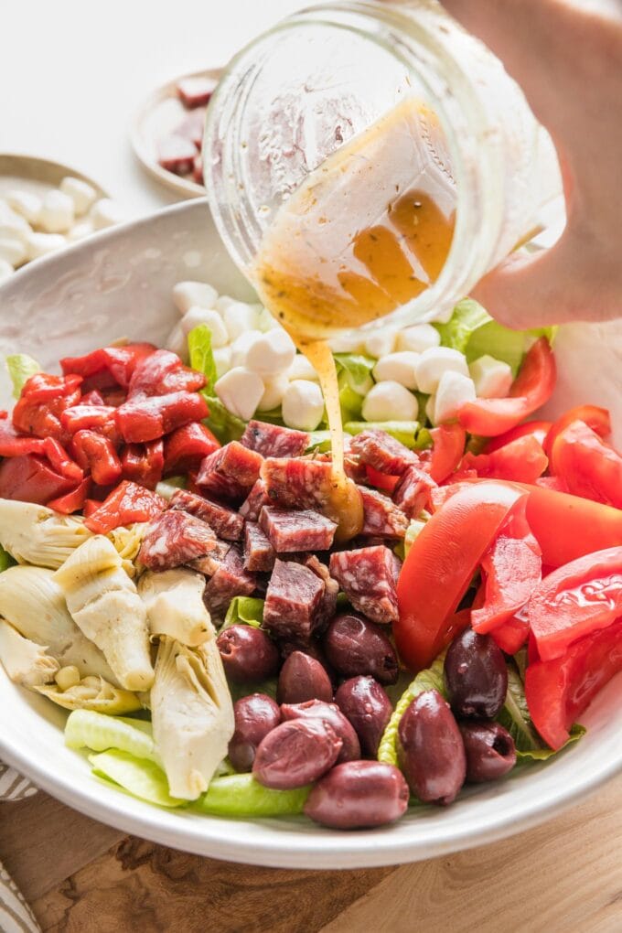 Close up of dressing being poured out of a small jar onto an antipasto salad.