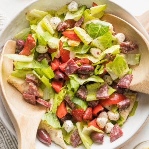 Large white bowl full of a tossed Italian antipasto salad.