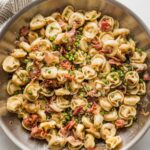 Large skillet full of brown butter bacon tortellini cooked with shallot, Parmesan, and peas.