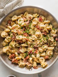 Large skillet full of brown butter bacon tortellini cooked with shallot, Parmesan, and peas.