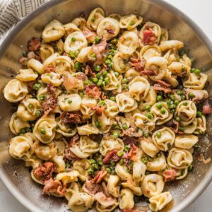 Large skillet full of brown butter bacon tortellini cooked with shallot, Parmesan, and peas.