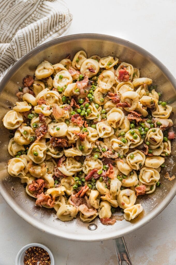 Large skillet full of brown butter bacon tortellini cooked with shallot, Parmesan, and peas.