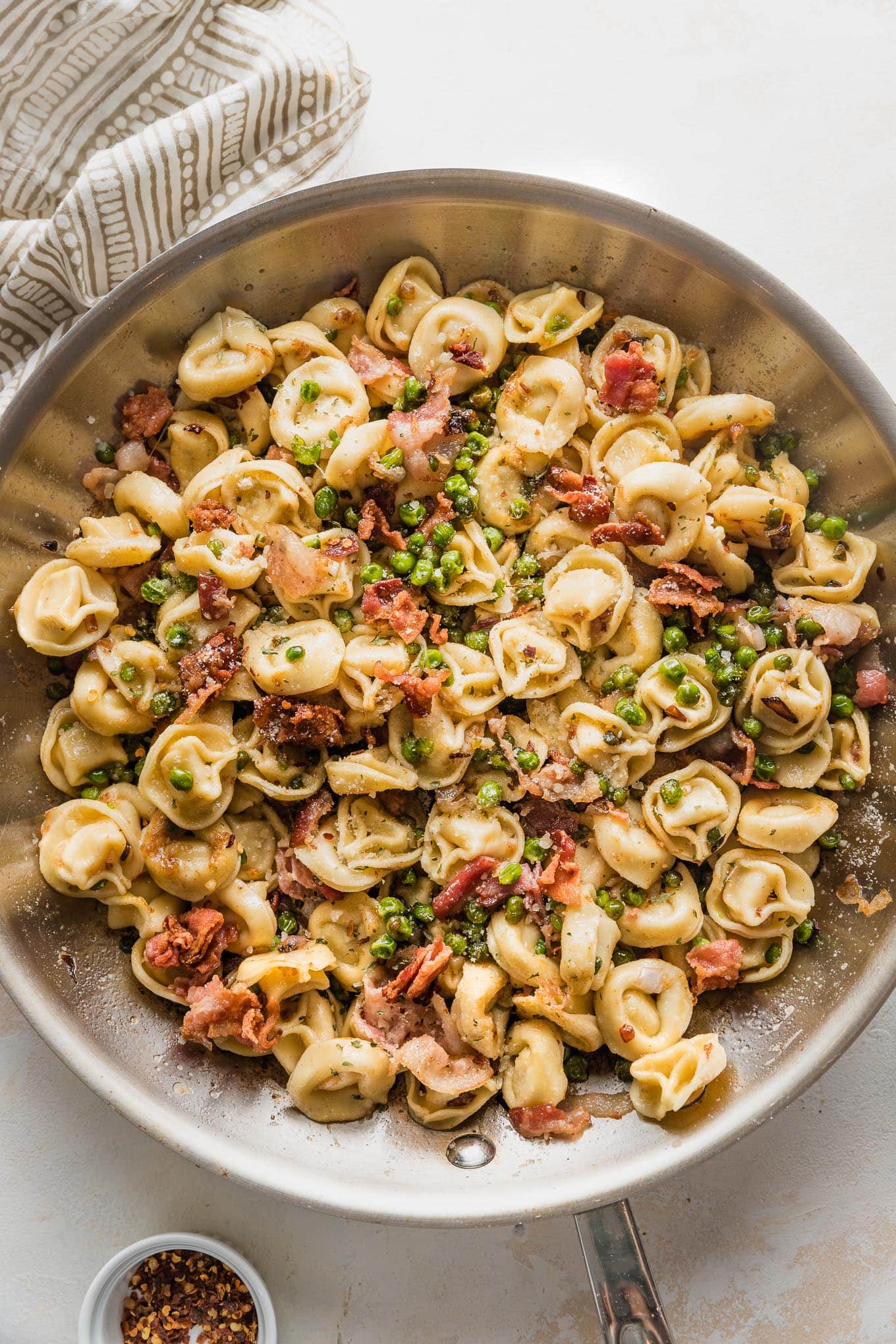 Large skillet full of brown butter bacon tortellini cooked with shallot, Parmesan, and peas.