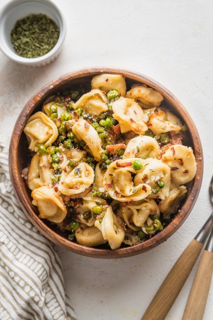Small serving bowl filled with brown butter bacon tortellini, peas, and Parmesan.