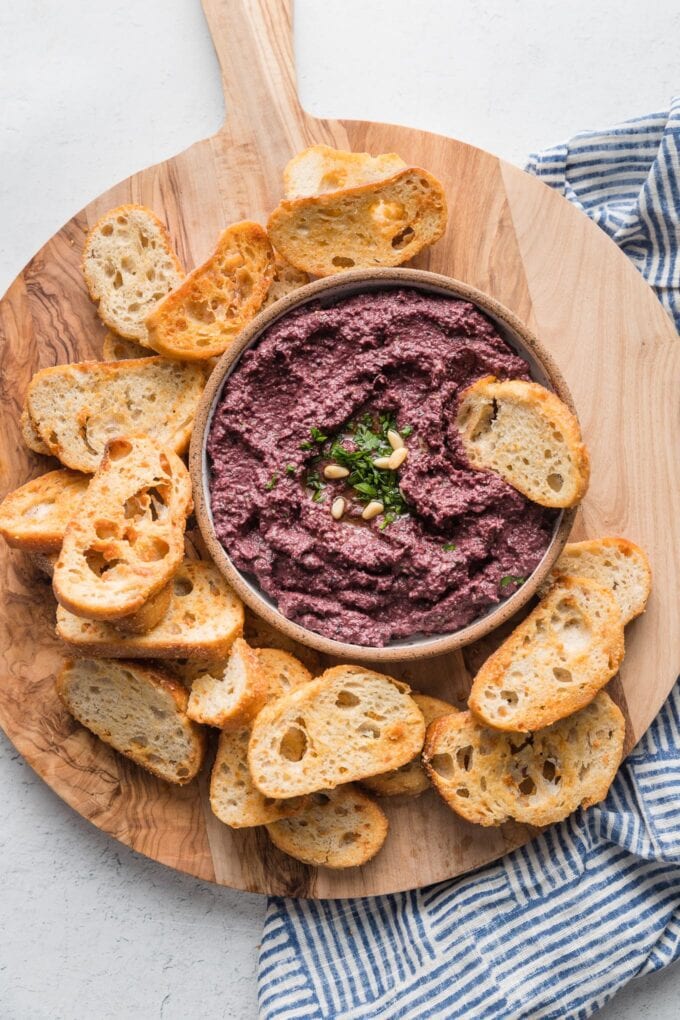 Olive wood cutting board with a bowl of olive tapenade surrounded by garlic crostini for dipping.