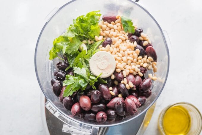 Olives, pine nuts, parsley, garlic, and lemon juice about to be blitzed in the bowl of a food processor.