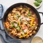 Deep cast iron skillet filled with tortellini, sausage, peppers, tomatoes, and Parmesan.