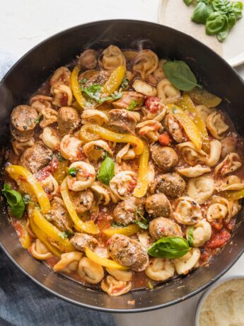 Large cast iron skillet filled with a one pot meal of cheese tortellini, Italian sausage, and bell peppers.