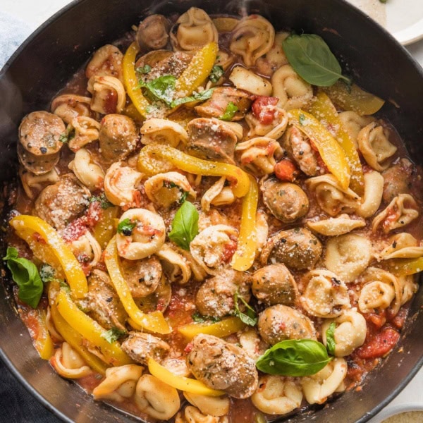 Large cast iron skillet filled with a one pot meal of cheese tortellini, Italian sausage, and bell peppers.