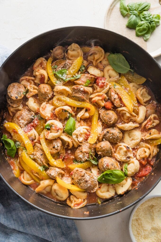 Large cast iron skillet filled with a one pot meal of cheese tortellini, sliced Italian sausage, and bell peppers.