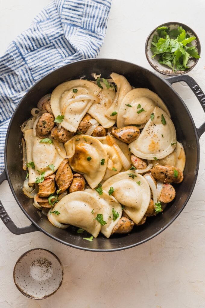 Table set with a large skillet of pierogies and sausage, onions, parsley, extra salt and pepper.