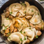 Large cast iron skillet filled with pierogies, chicken sausage, onions, and a butter sauce.