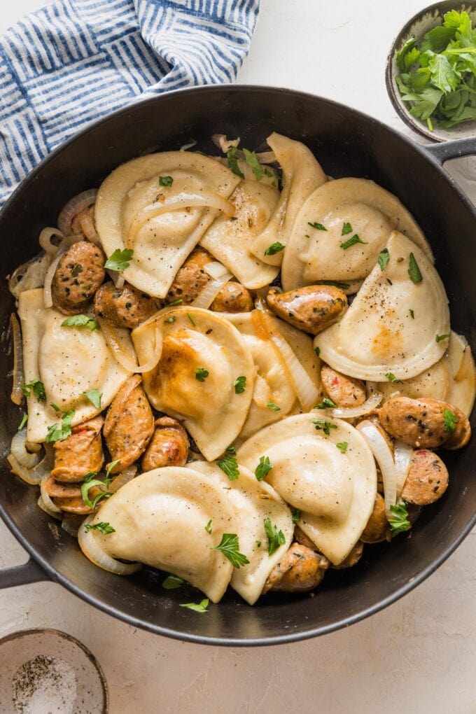 Large cast iron skillet filled with pierogies, chicken sausage, onions, and a butter sauce.