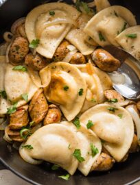 Close up of cooked pierogies with sausage and a light butter sauce in a skillet.