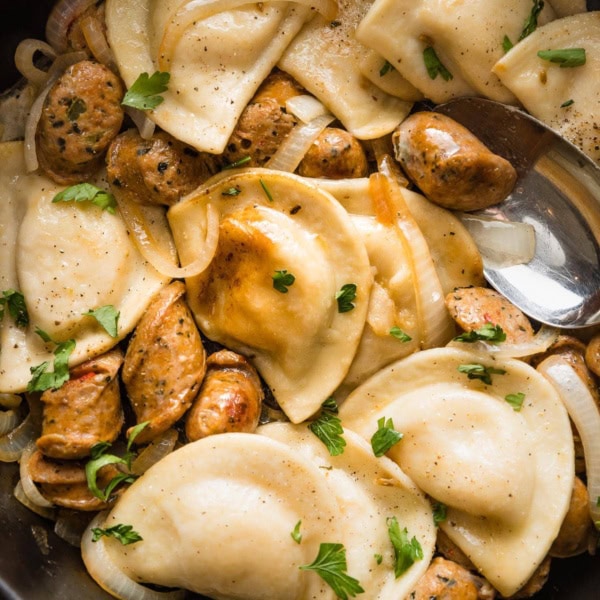 Close up of cooked pierogies with sausage and a light butter sauce in a skillet.