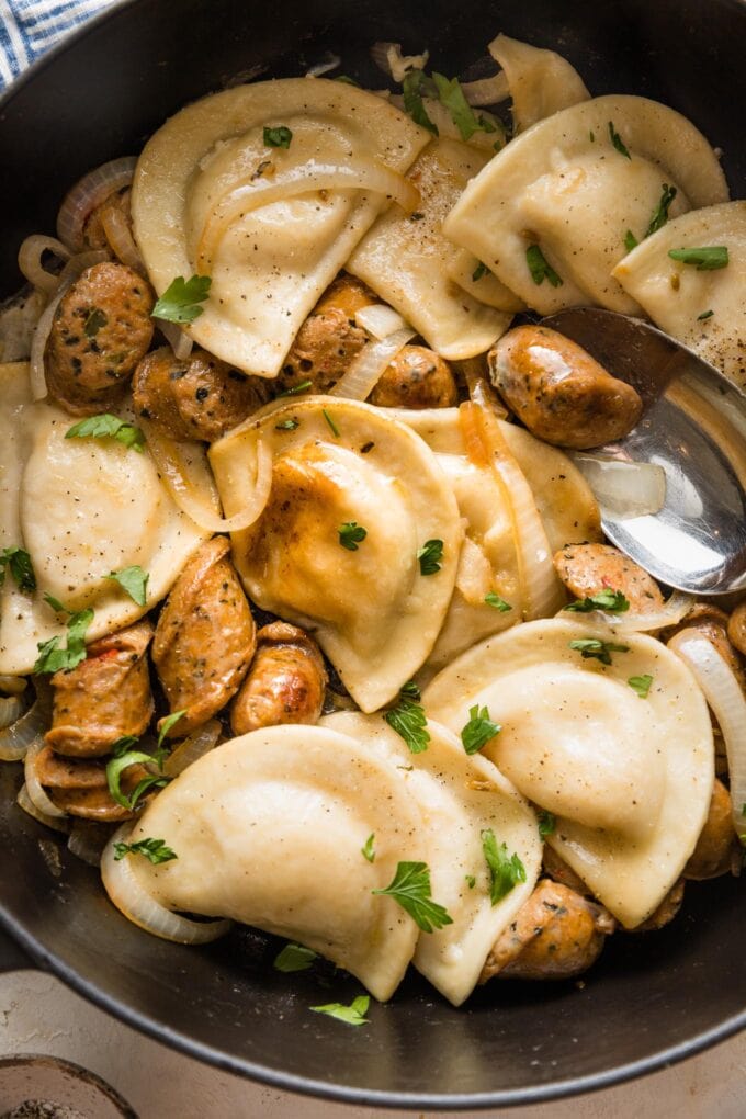 Close up of cooked pierogies with sausage and a light butter sauce in a skillet.