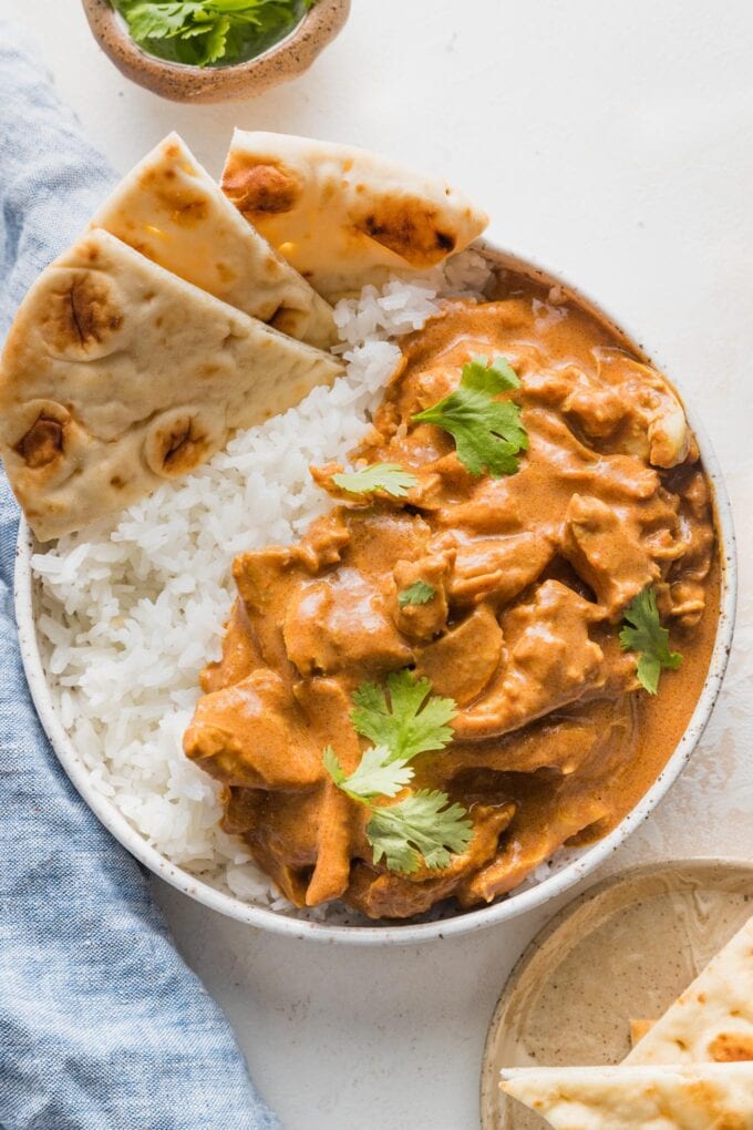 Crockpot butter chicken served in a small white bowl with naan and rice.