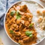 Bowl full of slow cooker butter chicken served with white rice, naan, and fresh cilantro.