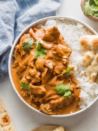 Bowl full of slow cooker butter chicken served with white rice, naan, and fresh cilantro.