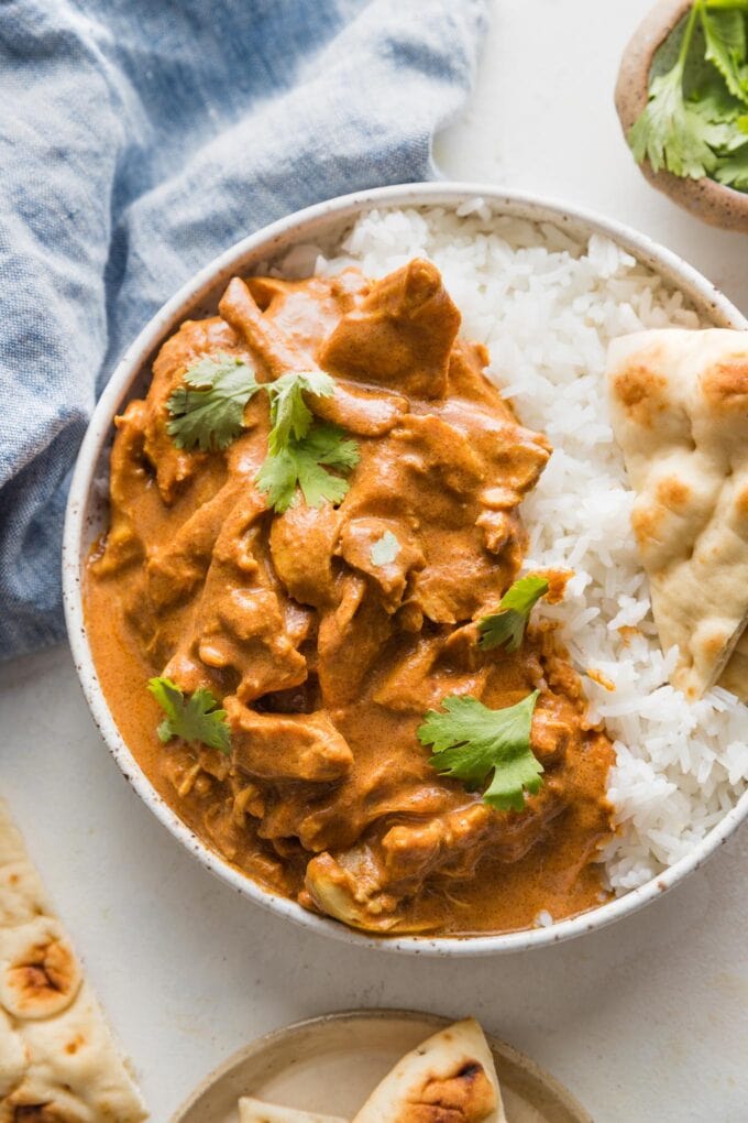 Bowl full of slow cooker butter chicken served with white rice, naan, and fresh cilantro.