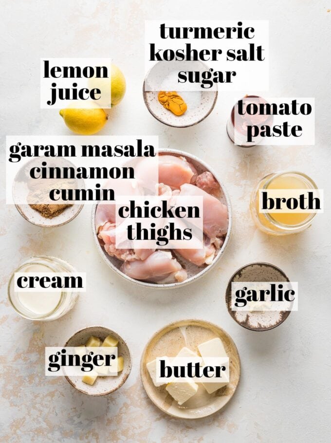 Labeled overhead photo of chicken thighs, broth, cream, butter, ginger, garlic, lemons, tomato paste, turmeric, kosher salt, sugar, garam masala, cinnamon, and cumin, all measured into prep bowls and ready to cook.