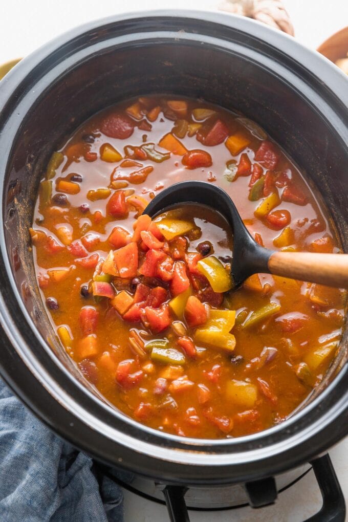 Angled view of a black ladle scooping pumpkin chili out of a large Crockpot.