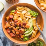 Small orange ceramic bowl filled with a helping of slow cooker pumpkin chili topped with corn chips, avocado, and cilantro.