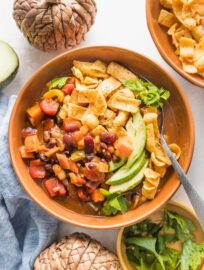 Small orange ceramic bowl filled with a helping of slow cooker pumpkin chili topped with corn chips, avocado, and cilantro.