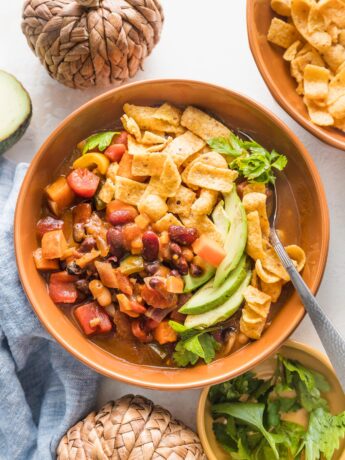 Small orange ceramic bowl filled with a helping of slow cooker pumpkin chili topped with corn chips, avocado, and cilantro.