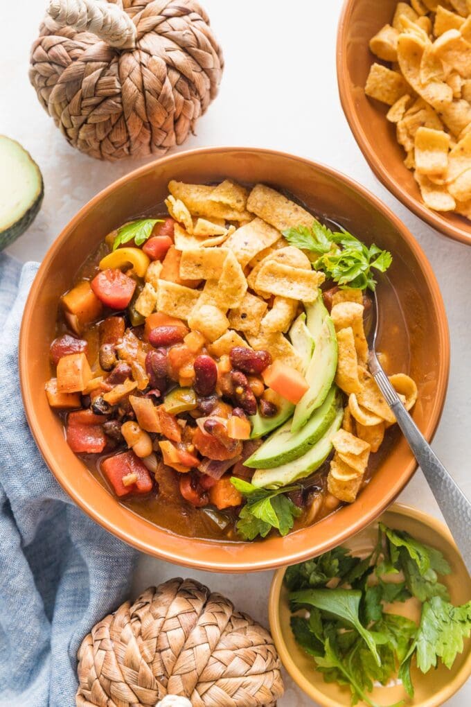 Small orange ceramic bowl filled with a helping of slow cooker pumpkin chili topped with corn chips, avocado, and cilantro.