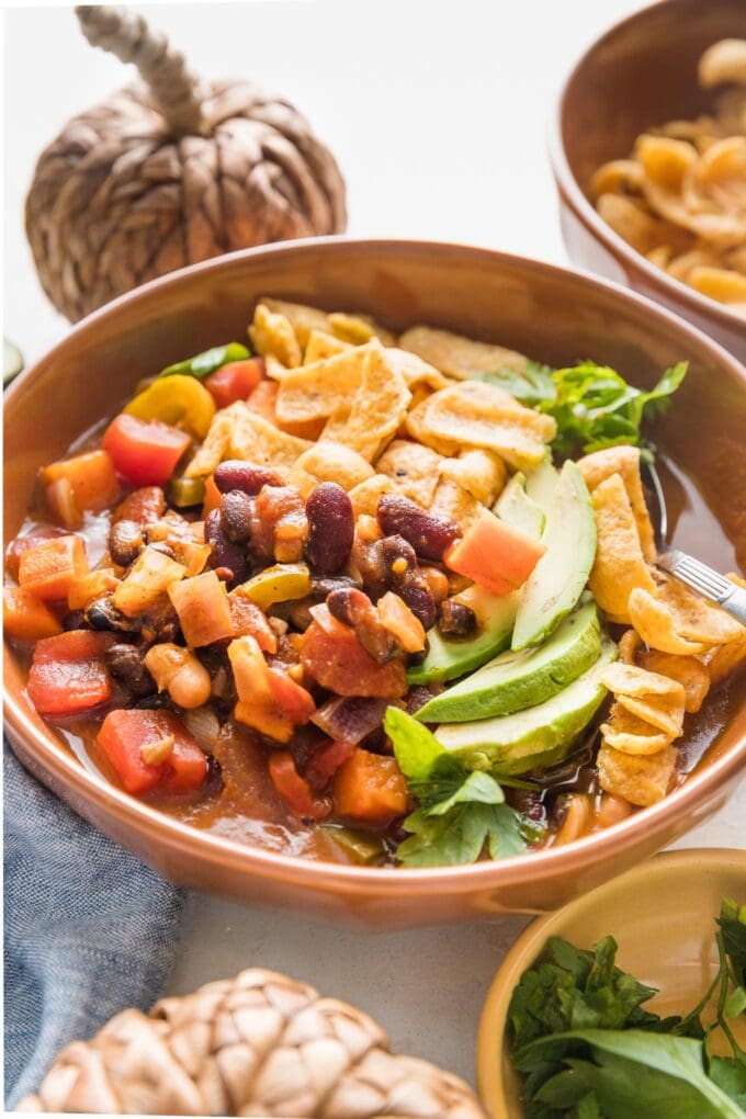 Side view of an orange bowl filled with slow cooker pumpkin chili topped with avocado and Fritos.