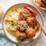 Small bowl filled with a helping of chicken meatballs in tomato sauce with bell peppers and orzo.