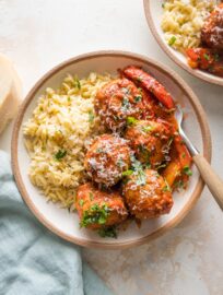 Small bowl filled with a helping of chicken meatballs in tomato sauce with bell peppers and orzo.