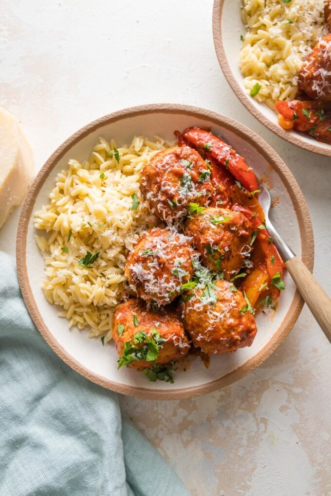 Small bowl filled with a helping of chicken meatballs in tomato sauce with bell peppers and orzo.
