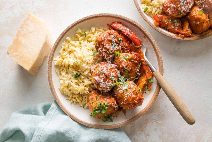 Landscape image of chicken meatballs with orzo and peppers served in a bowl with extra grated Parmesan.
