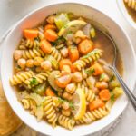 Bowl full of chickpea noodle soup with vegetables, broth, and parsley.