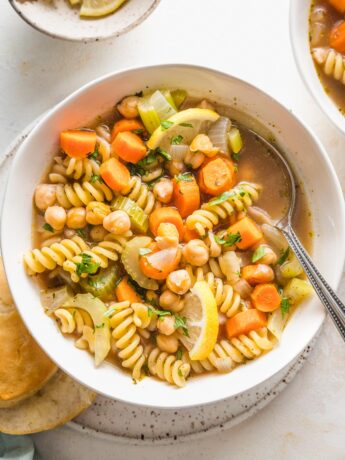 Bowl full of chickpea noodle soup with vegetables, broth, and parsley.