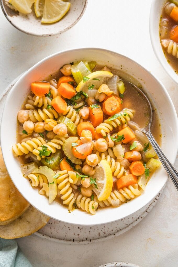 Bowl full of chickpea noodle soup with vegetables, broth, and parsley.