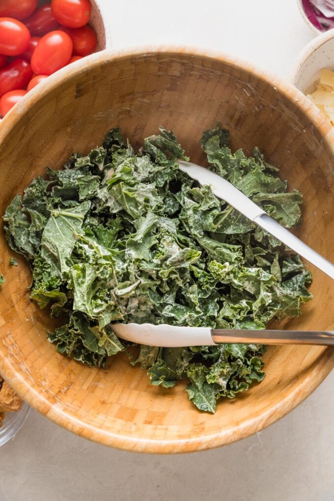 Shredded kale being massaged in a bowl with Caesar dressing.