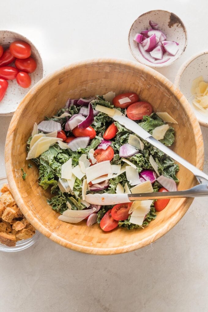 Cherry tomatoes, Parmesan, and red onion added to kale in a large salad bowl.